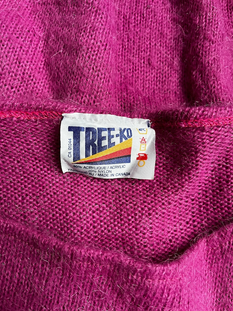 May include: A purple sweater with a white label that reads "TREE-KO" and includes care instructions. The label says "80% Acrylic/Acrylic 20% Nylon" and "Fabrique au/Made in Canada".