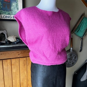 May include: A pink fluffy sleeveless sweater with a round neckline. The sweater is on a mannequin and is paired with a black leather skirt.