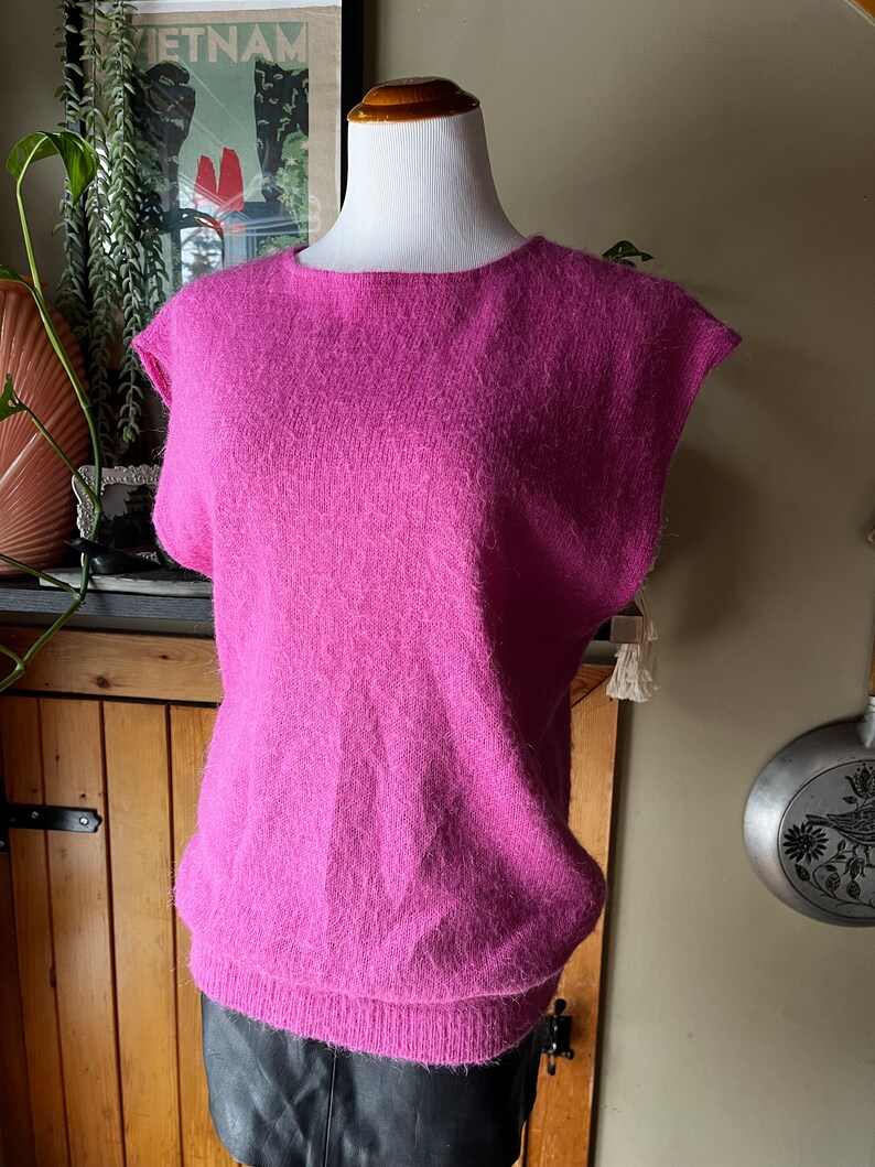 May include: A fluffy pink sleeveless sweater with a round neckline. The sweater is made of a soft, fluffy material.