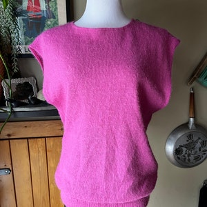 May include: A pink fluffy sleeveless sweater with a round neckline.
