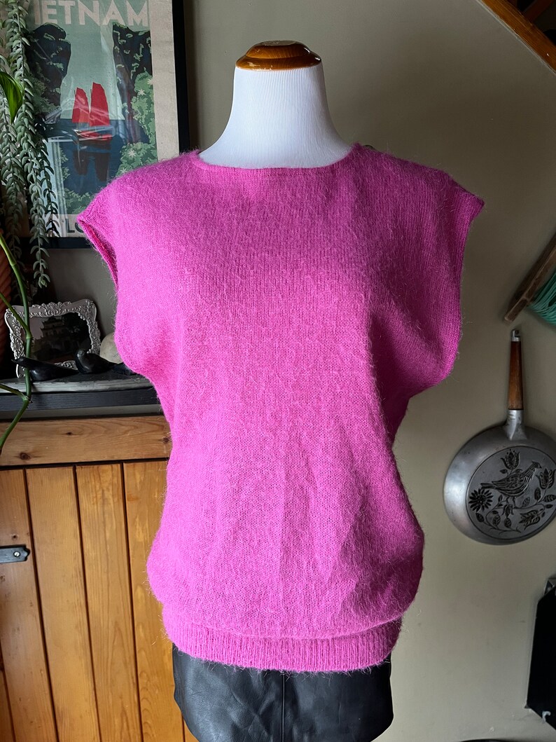 May include: A pink fluffy sleeveless sweater with a round neckline.
