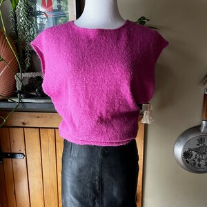 May include: A pink fluffy sleeveless sweater with a black leather skirt.