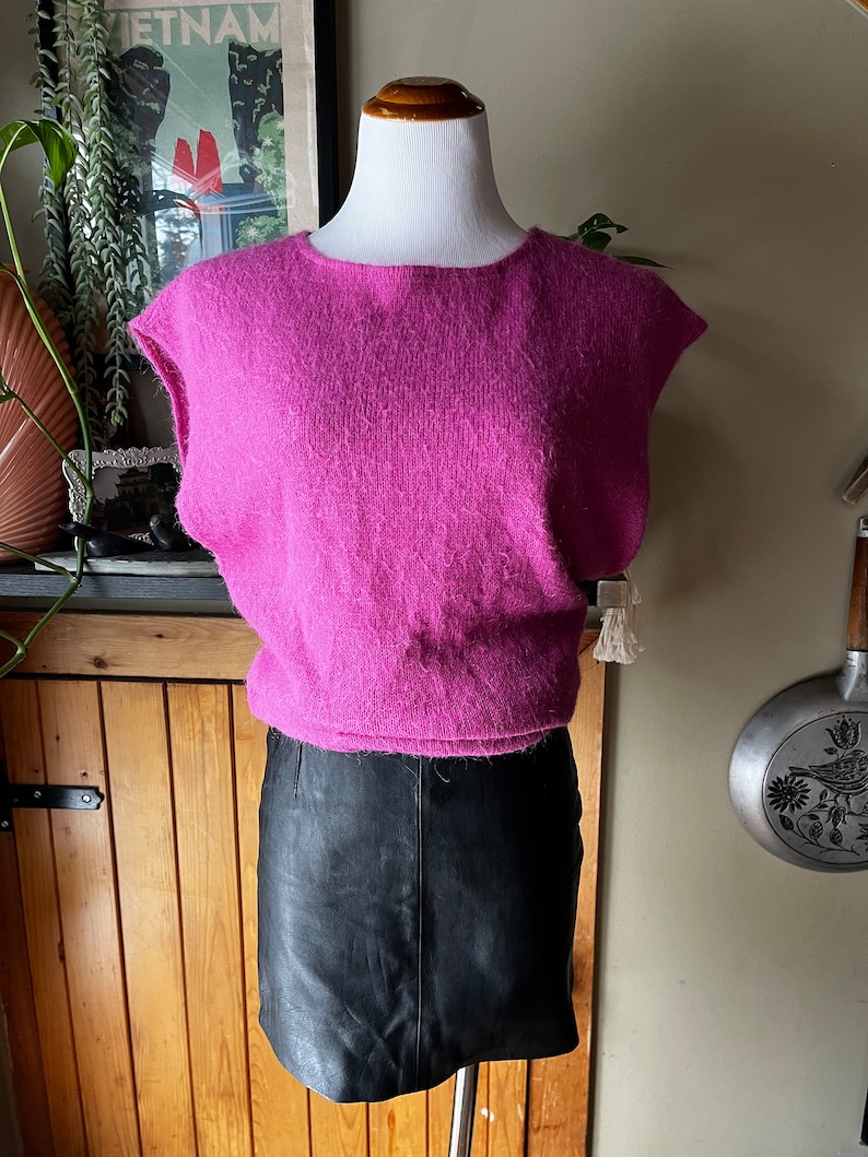 May include: A pink fluffy sleeveless sweater with a black leather skirt.