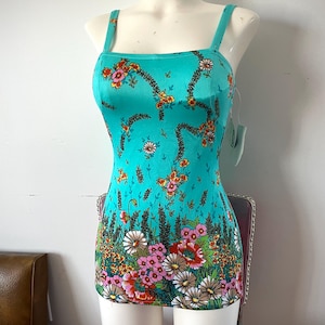 May include: A turquoise floral print dress with a square neckline and spaghetti straps. The dress features a vibrant floral pattern in shades of pink, orange, and white. The dress is displayed on a mannequin.