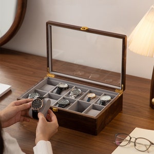 May include: A wooden watch box with a glass top and multiple compartments for storing watches. The box is open and several watches are visible inside.