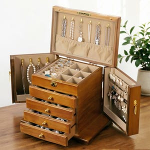 May include: A wooden jewelry box with multiple compartments and drawers. The box is open, revealing necklaces, rings, and earrings. The interior is lined with a beige fabric. The box has a warm, natural wood finish and gold-colored hardware.