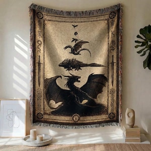May include: A woven tapestry featuring a dragon design in black against a beige background. The artwork depicts three dragons of varying sizes, with swords and runes framing the image. The tapestry has a fringed edge.