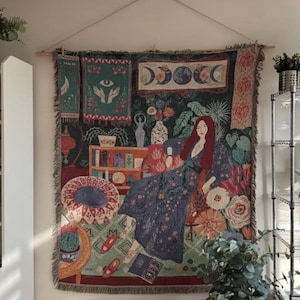 Könnte beinhalten: Wandteppich mit einer Frau mit langen roten Haaren in einem floral gemusterten Kleid. Der Wandteppich zeigt Bilder der Mondphasen, Hände und ein Auge. Die Farbpalette umfasst Blau-, Grün-, Rot- und Brauntöne.