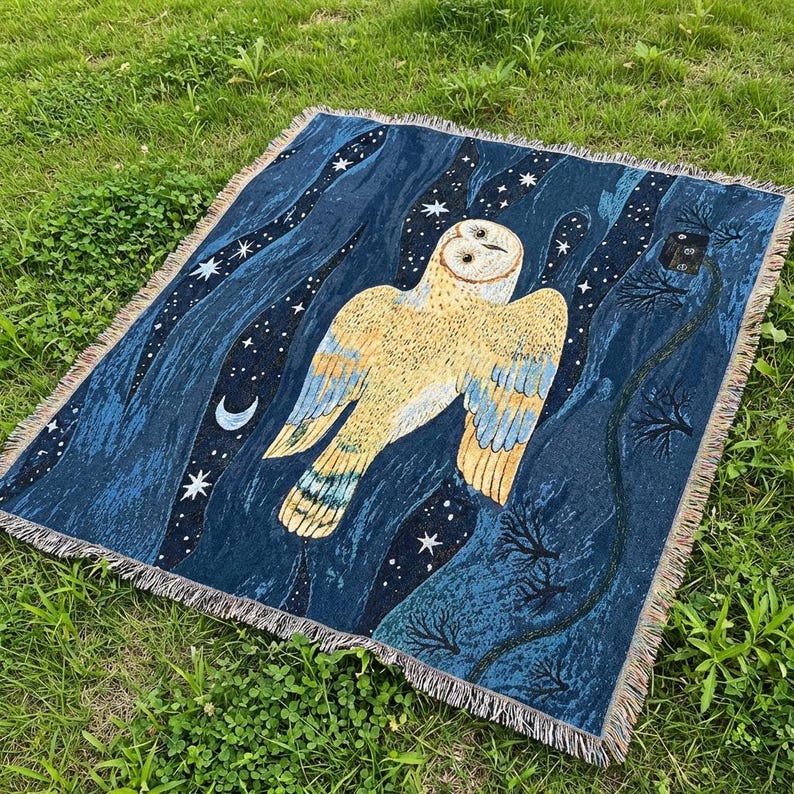 May include: A woven throw blanket featuring a large owl design against a dark blue night sky with stars and a crescent moon. The owl is primarily yellow and tan with blue wing accents. The blanket has a fringed edge.