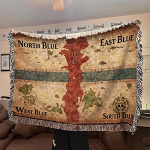 Può includere: Una coperta tessuta con un disegno a mappa. La mappa presenta i testi "North Blue", "East Blue", "West Blue" e "South Blue". Una massa terrestre rossa è etichettata "Red Line", ed è visibile un emblema di teschio e ossa incrociate.