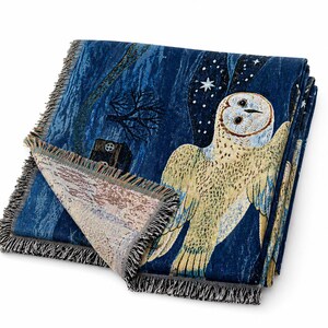 May include: A folded blue throw blanket with a detailed owl design. The blanket features a night scene with an owl, stars, and a tree. The edges are finished with a fringe.