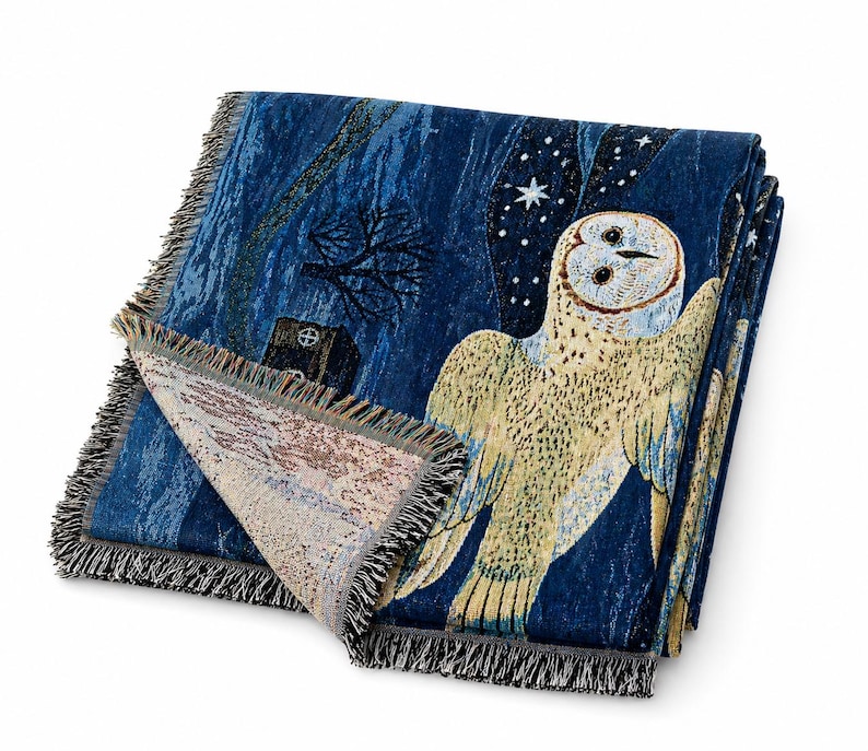 May include: A folded blue throw blanket with a detailed owl design. The blanket features a night scene with an owl, stars, and a tree. The edges are finished with a fringe.