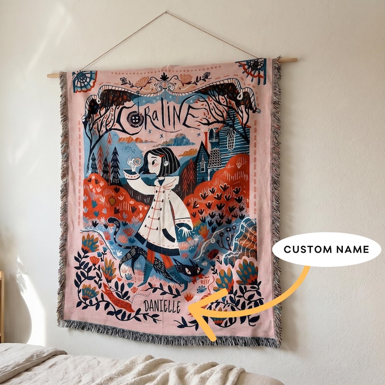 Puede incluir: Un tapiz rosa tejido con una ilustraci&oacute;n de fantas&iacute;a, con el nombre "Coraline". La obra de arte representa a una ni&ntilde;a con un abrigo blanco, un gato negro y una escena de bosque estilizada. El nombre "Danielle" est&aacute; impreso en la parte inferior.