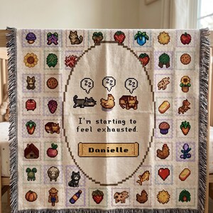 Op de afbeelding: Een beige sprei met een gepixeld ontwerp met verschillende boerderij-thema-iconen en de tekst "I'm starting to feel exhausted." De sprei heeft een gefranjerde rand en bevat de naam "Danielle".