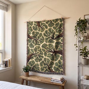 May include: A rectangular woven tapestry featuring a repeating pattern of tree canopies viewed from below, with dark brown trunks and branches against a cream background, finished with a fringed edge and suspended from a wooden rod with string.