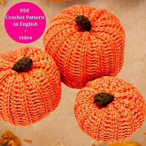 May include: Three crocheted pumpkins in shades of orange. The pumpkins are made with a textured stitch and have a brown stem.