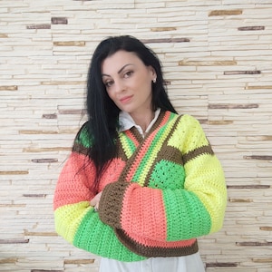 Op de afbeelding: Een kleurrijk gebreid vest met een bruin, groen, roze en geel gestreept patroon. Het vest is open aan de voorkant en heeft een V-hals.