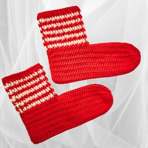 May include: A pair of red crochet slippers with white and red striped cuffs. The slippers are handmade and appear soft and comfortable. The background is a soft white fabric.
