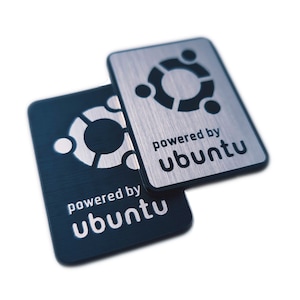 Peut inclure: Deux autocollants en métal noir et argent avec le logo Ubuntu et le texte "powered by ubuntu".