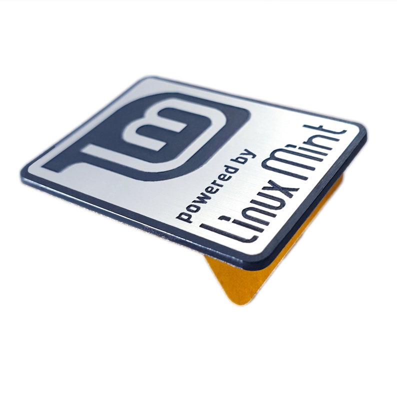 May include: A silver metal sticker with a blue Linux Mint logo and the text "Powered by Linux Mint".