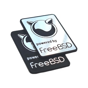 Puede incluir: Dos pegatinas, una plateada y otra negra, con el logotipo de FreeBSD y el texto "powered by FreeBSD".