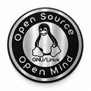 Könnte beinhalten: Ein kreisförmiges Metallemblem mit gebürsteter Silberoptik und schwarzen Akzenten. In der Mitte ist das Tux-Pinguin-Maskottchen über dem Text GNU/Linux abgebildet. Der äußere Ring trägt die erhabene silberne Aufschrift Open Source und Open Mind.