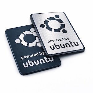Könnte beinhalten: Zwei rechteckige Metallschilder mit dem Ubuntu-Logo und dem Schriftzug "powered by ubuntu". Ein Schild hat eine gebürstete silberne Oberfläche mit schwarzem Logo und Text, das andere eine dunkelgraue Oberfläche mit silbernem Logo und Text.