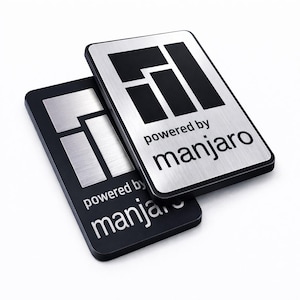 May include: Two rectangular metal badges with a brushed silver finish and black borders. Each badge features a black geometric logo at the top and the text "powered by manjaro" printed in black below the logo. The badges are stacked slightly offset.