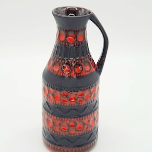 Puede incluir: Un jarrón de cerámica negro y rojo con un patrón geométrico. El jarrón tiene un cuerpo redondeado y una pequeña asa.