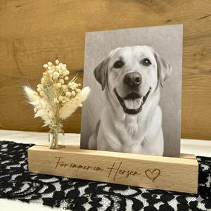 Könnte beinhalten: Ein Holz-Fotorahmen mit einem Schwarz-Weiß-Bild eines lächelnden Hundes. Der Halter hat den Text "Für immer im Herzen" und ein Herzsymbol. Links vom Foto befindet sich eine kleine Glasvase mit Trockenblumen.