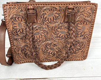 May include: A brown leather tote bag with a braided handle and a floral tooled design. The bag has a zipper closure and a detachable shoulder strap.