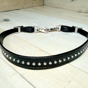 May include: Black leather belt with silver-tone hardware and clear rhinestone accents. The belt features a lobster clasp closure and rectangular belt loops. The rhinestones are evenly spaced along the belt's length.