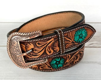 Peut inclure: Une ceinture en cuir marron avec une boucle argentée et des motifs floraux turquoise. La ceinture est enroulée et la boucle est face à l'appareil photo.