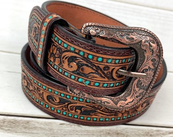 Peut inclure: Une ceinture en cuir marron avec une boucle ton cuivre. La ceinture est décorée de points turquoise et d'un motif floral complexe.