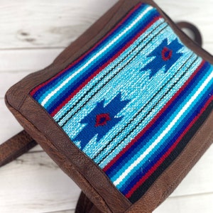 May include: A brown leather backpack with a blue, red, and white woven pattern on the front flap.
