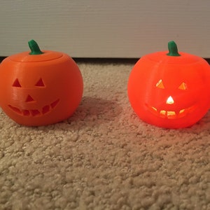 May include: Three orange jack-o'-lantern candle holders with green stems. The middle jack-o'-lantern is lit and glowing.
