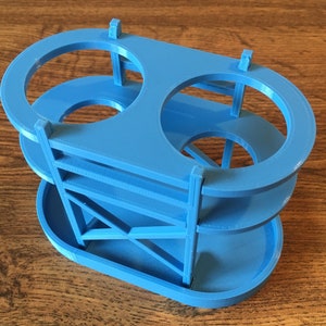 May include: A blue plastic two-tiered stand with two circular openings on the top tier and a rectangular base.
