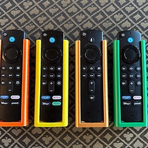 May include: Four different colored remote control holders for streaming devices. The holders are orange, yellow, orange, and green. The remotes are black and have buttons for Netflix, Hulu, Disney+, and Peacock.