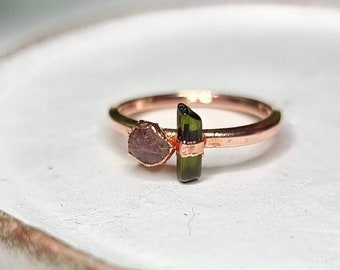 May include: A rose gold ring with a small, pink, raw gemstone and a green tourmaline gemstone.