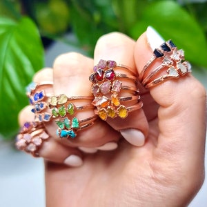 May include: A set of seven delicate gold rings, each featuring a different gemstone. The gemstones are arranged in a rainbow order, starting with red and ending with purple. The rings are stacked on top of each other, creating a colourful and eye-catching display.