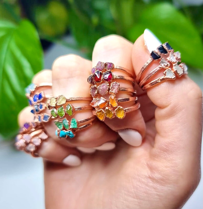 May include: A set of seven delicate gold rings, each featuring a different gemstone. The gemstones are arranged in a rainbow order, starting with red and ending with purple. The rings are stacked on top of each other, creating a colourful and eye-catching display.