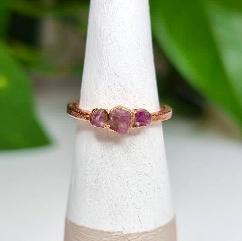 May include: A rose gold ring with three pink raw ruby stones set in the band.