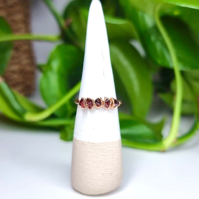 May include: A gold ring with a row of six small, red, raw garnet stones.