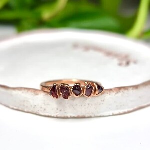May include: A gold ring with five small, irregular, dark red gemstones set in a row.