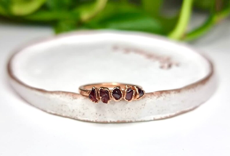 May include: A gold ring with five small, irregular, dark red gemstones set in a row.