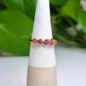 May include: A gold ring with five small, pink, raw ruby stones set in a row.
