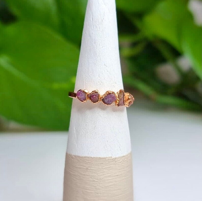 May include: A gold ring with five small, pink, raw ruby stones set in a row.