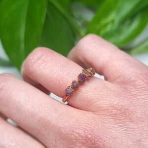 May include: A gold ring with a row of small, raw pink and purple gemstones.