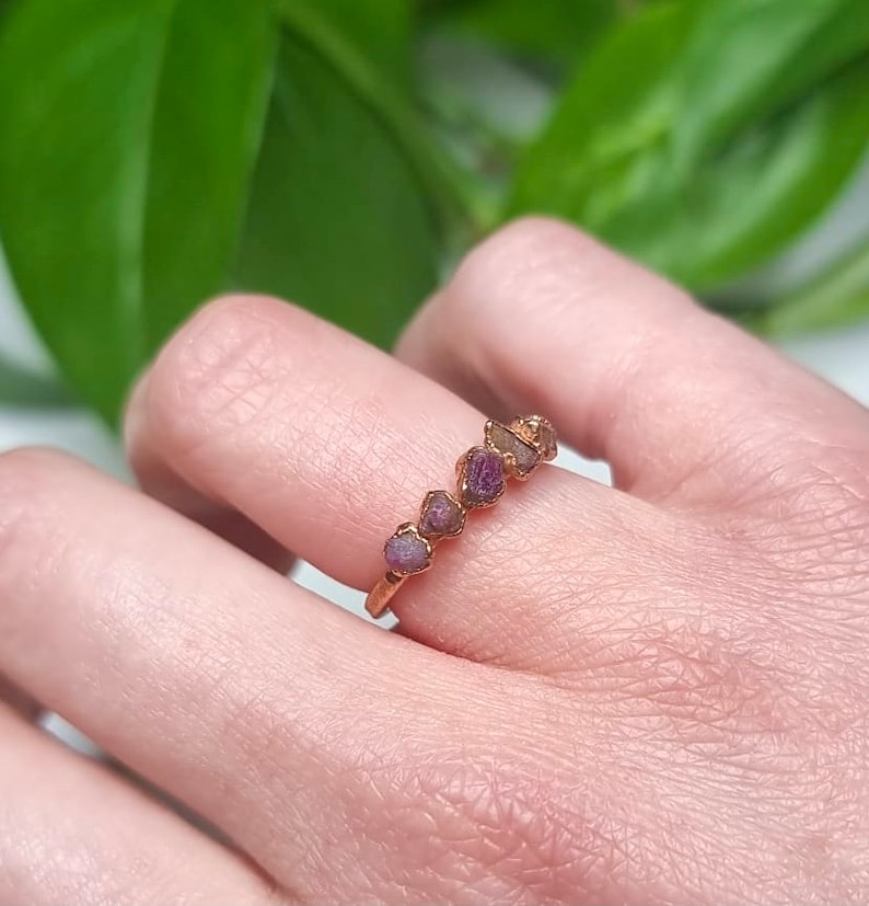 May include: A gold ring with a row of small, raw pink and purple gemstones.