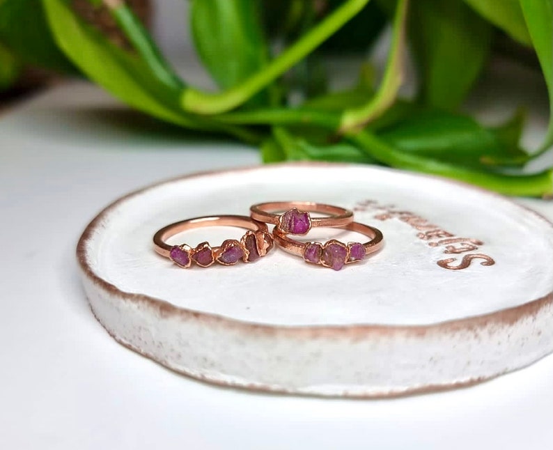 May include: Three rose gold rings with pink gemstone accents. The rings are stacked on a white ceramic dish.